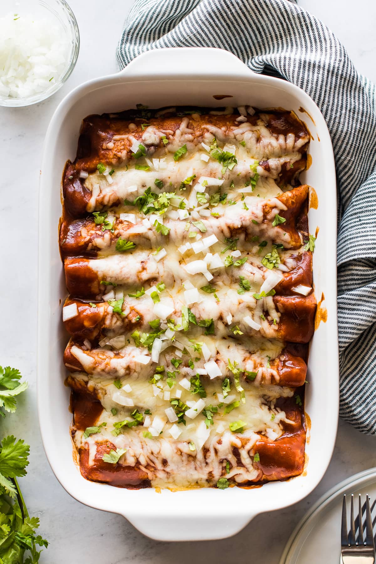 Turkey enchiladas in a baking dish topped with cilantro and onions.
