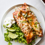 Turkey enchiladas on a plate with lettuce and sour cream.