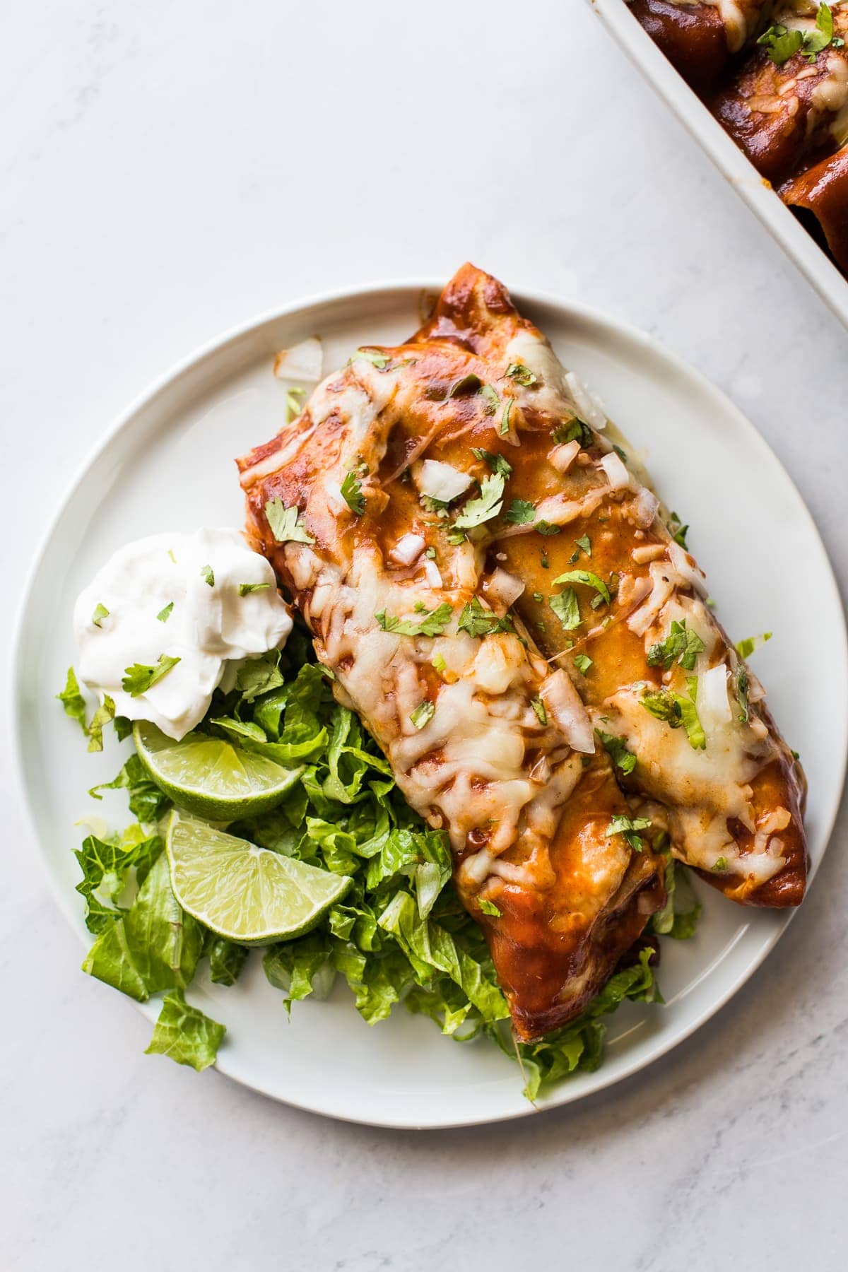 Turkey enchiladas on a plate with lettuce and sour cream.