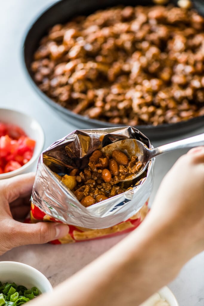 A hand adding filling to a bag of corn chips for walking tacos.