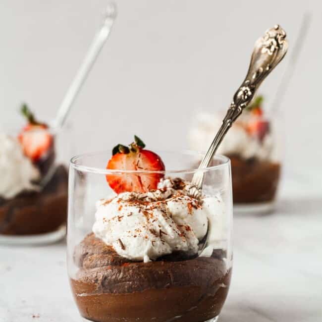 Avocado chocolate mousse in a cup topped with whipped cream and strawberries.