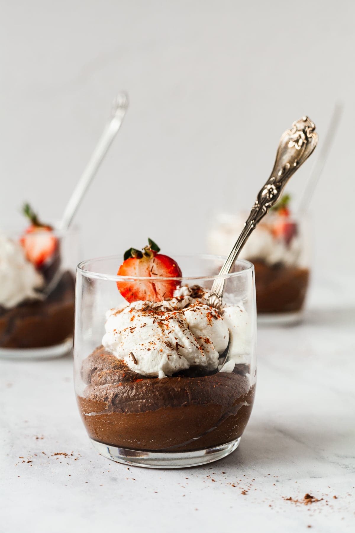 Avocado chocolate mousse in a cup topped with whipped cream and strawberries.