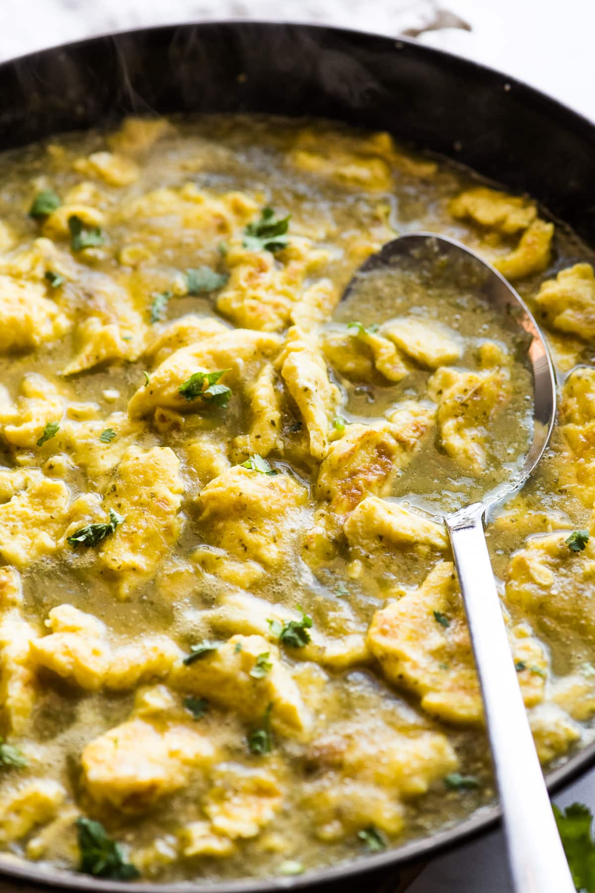 Scrambled eggs simmer in a salsa verde in a skillet.