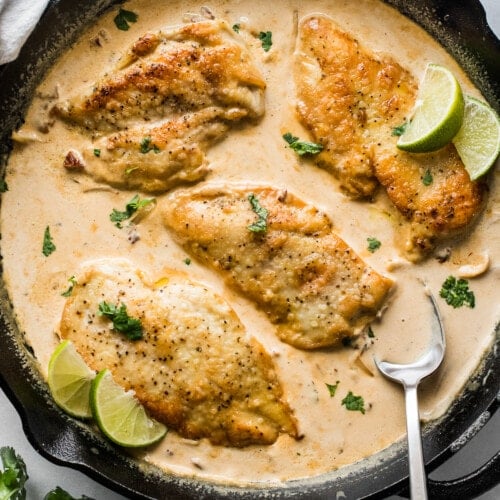 Pollo en Chipotle (Creamy Chipotle Chicken) in a skillet topped with cilantro and lime wedges.