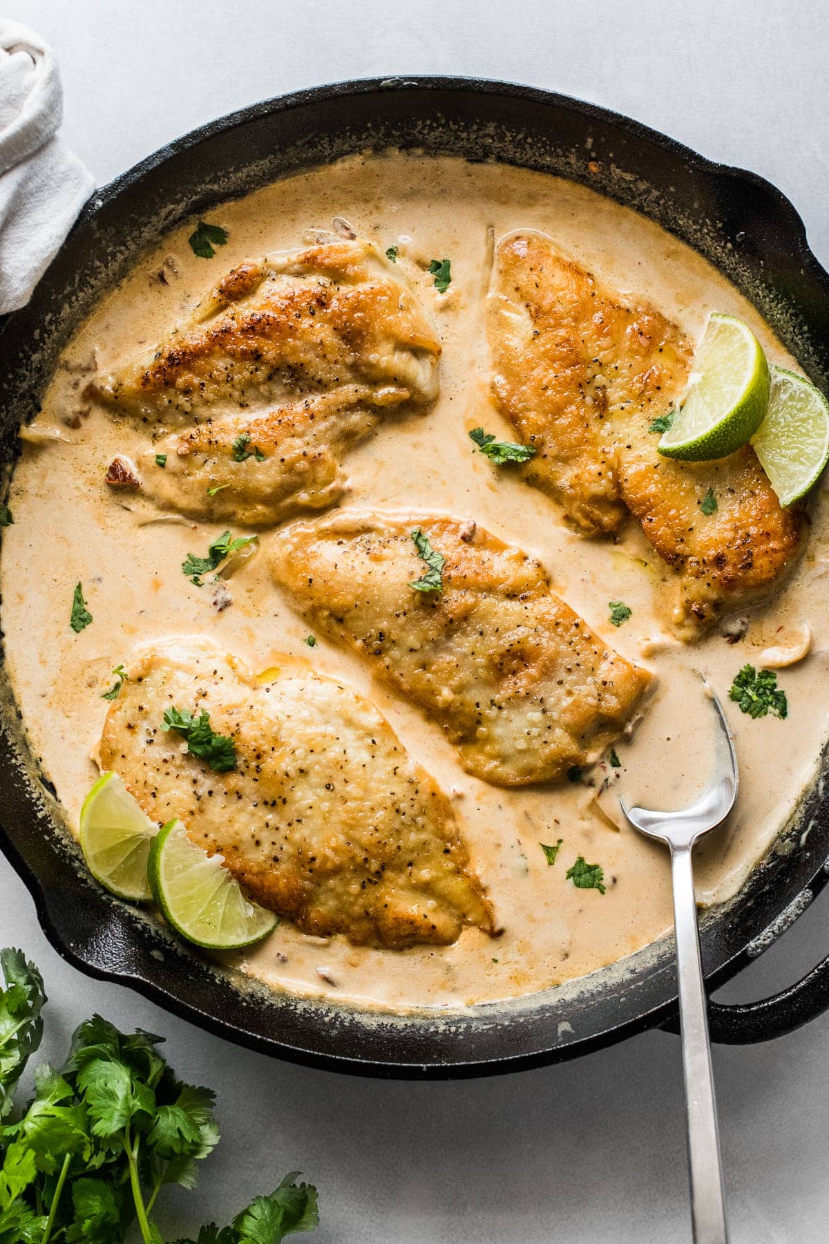 Pollo en Chipotle (Creamy Chipotle Chicken) in a skillet topped with cilantro and lime wedges.