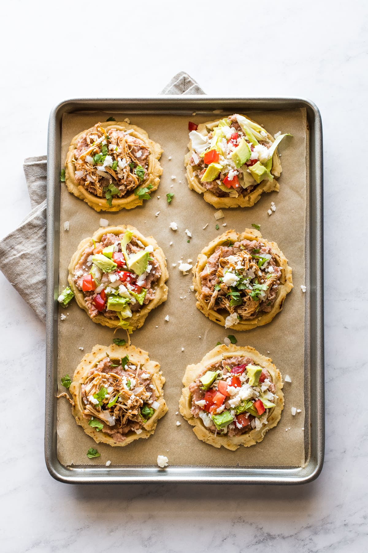 Mexican sopes topped with various toppings on a baking sheet.