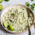 A bowl of cilantro lime cauliflower rice on a table next to fresh limes.