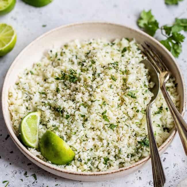 A bowl of cilantro lime cauliflower rice on a table next to fresh limes.