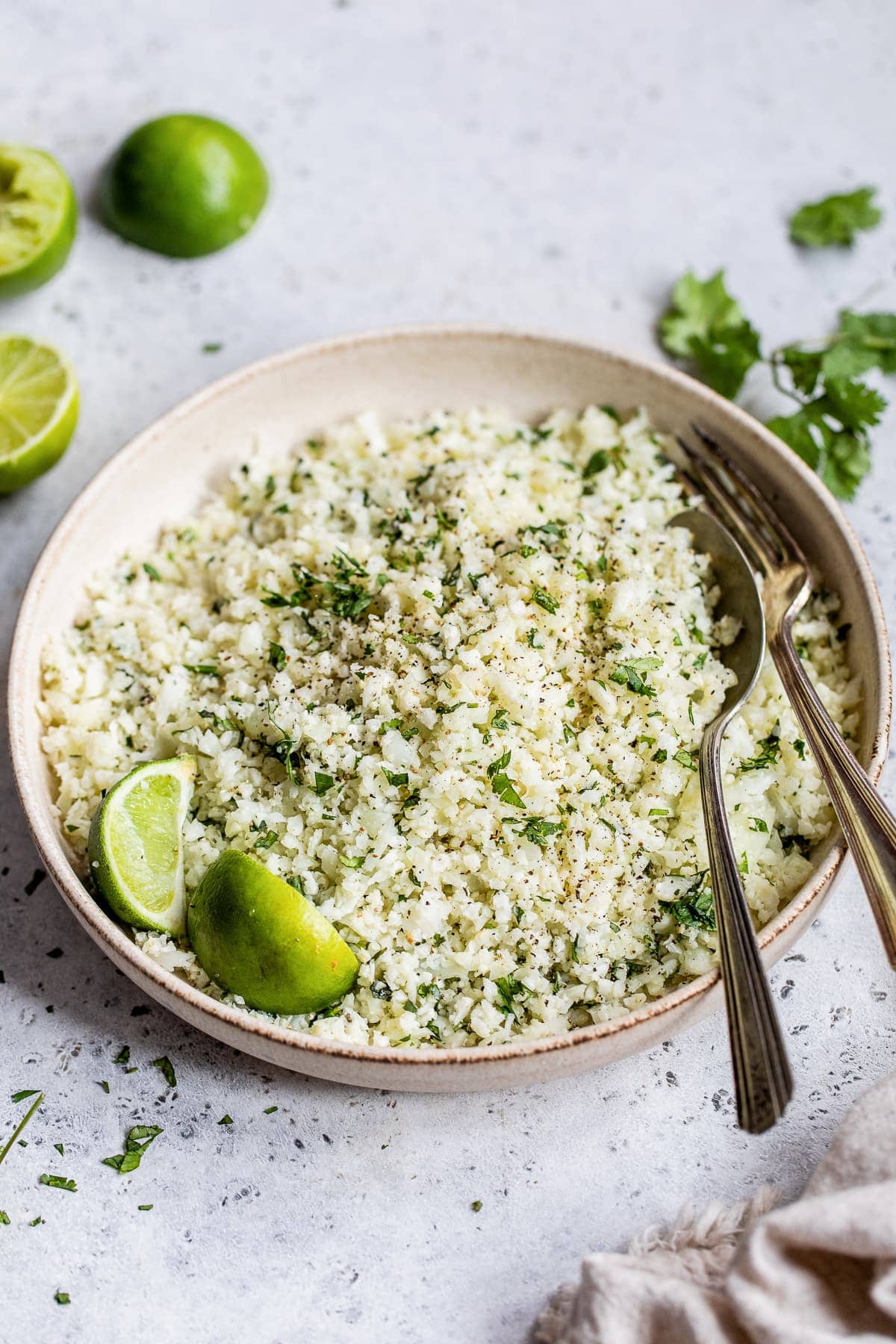 A bowl of cilantro lime cauliflower rice on a table next to fresh limes.