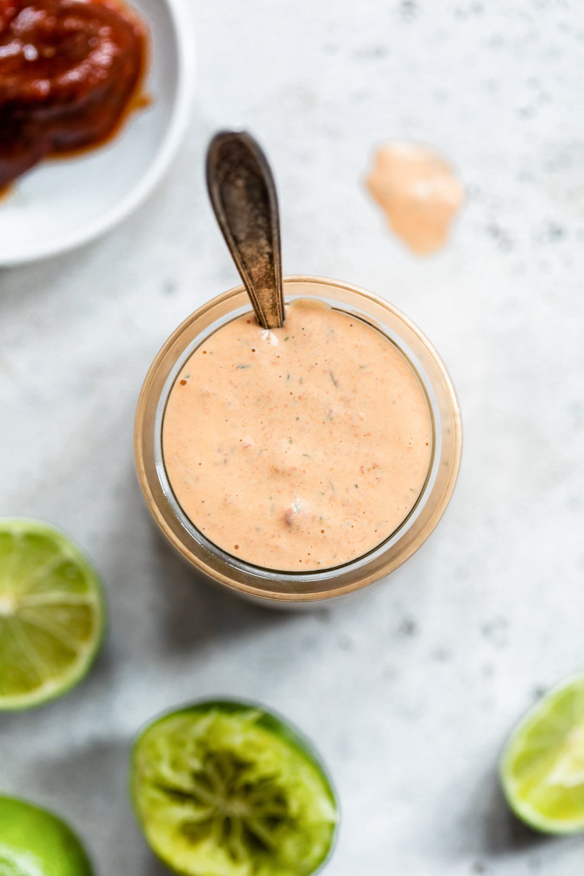 Chipotle ranch dressing in a jar with a spoon in it next to limes and chipotle peppers.