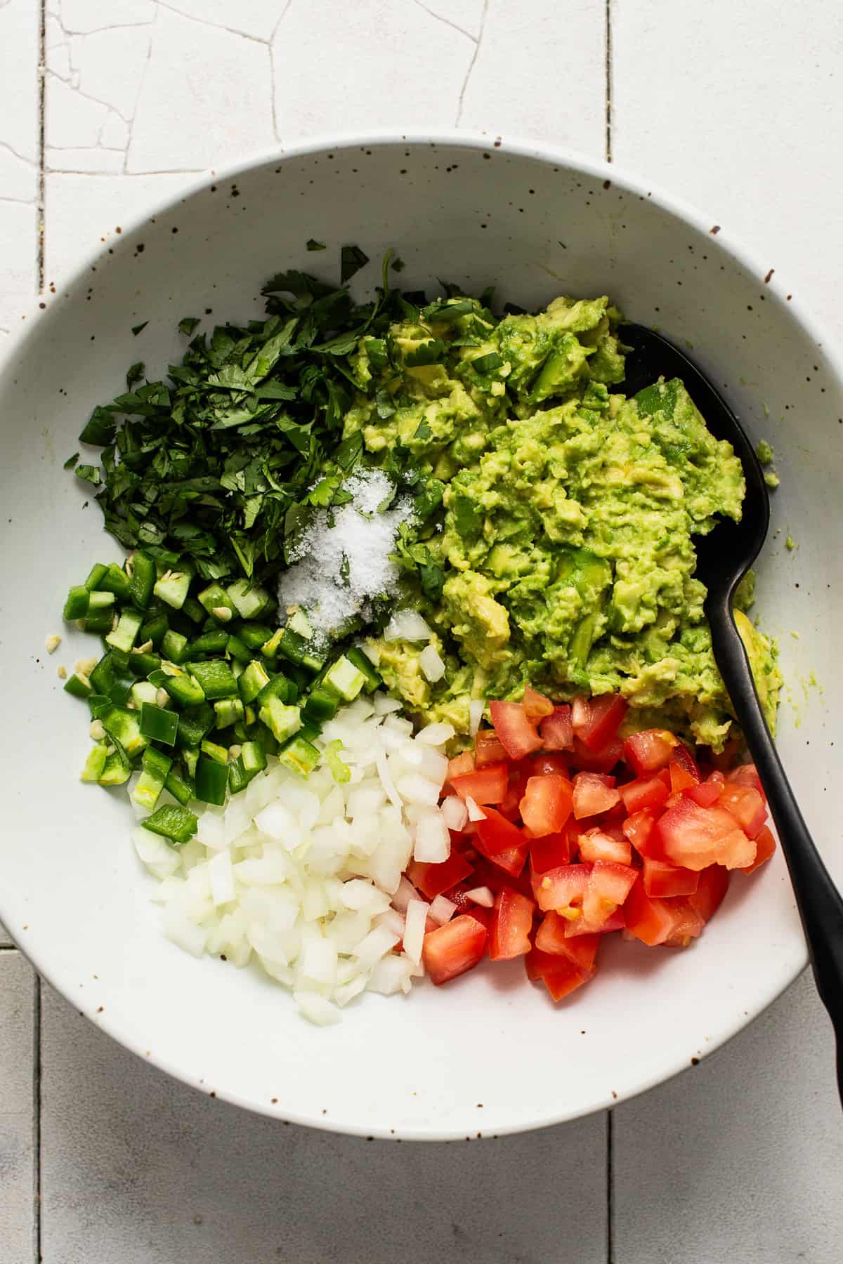 Smashed avocado, cilantro, jalapeño, onion, tomato, and salt in a bowl.