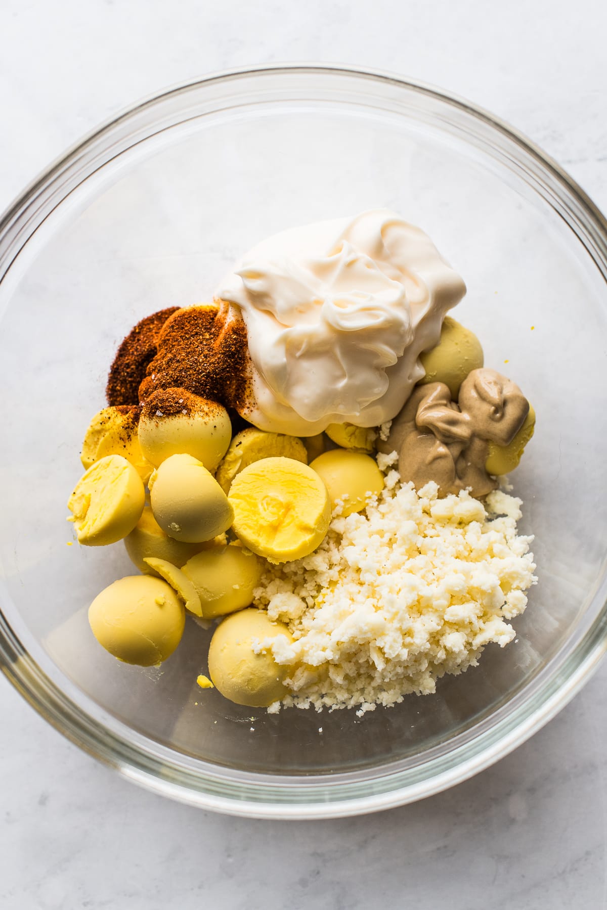 Cooked egg yolks, cotija cheese, mayonnaise, dijon mustard, and spices in a bowl.