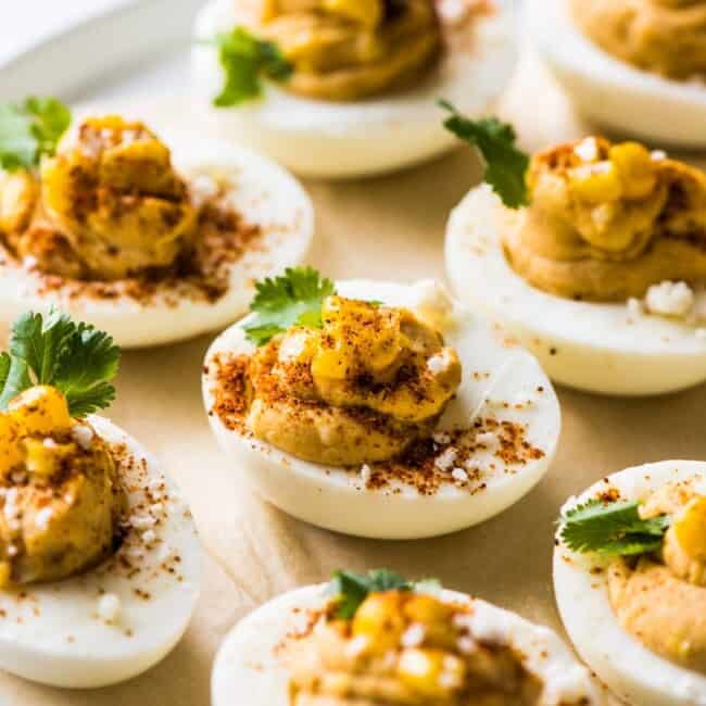 Mexican deviled eggs on a plate topped with corn, cilantro, chili powder, and cotija cheese.