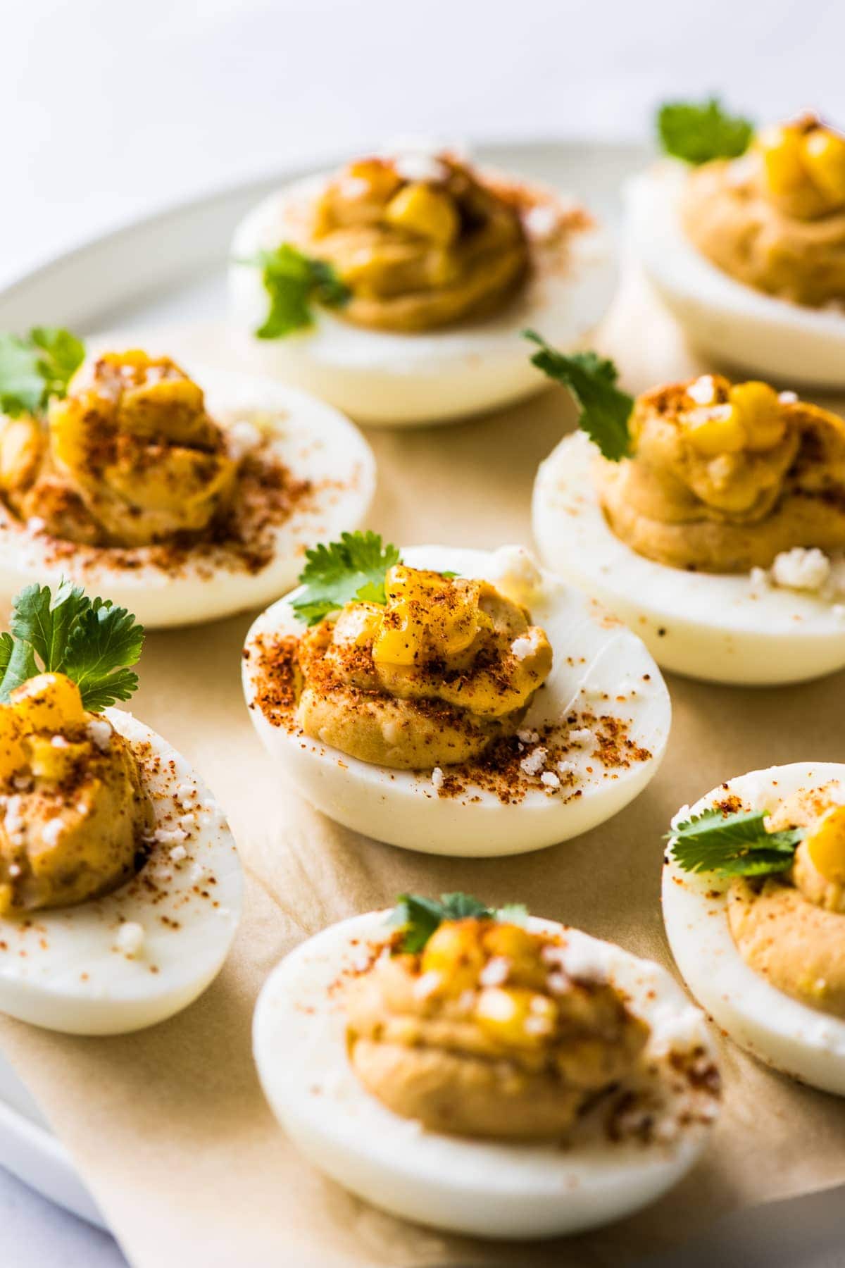 Mexican deviled eggs on a plate topped with corn, cilantro, chili powder, and cotija cheese.