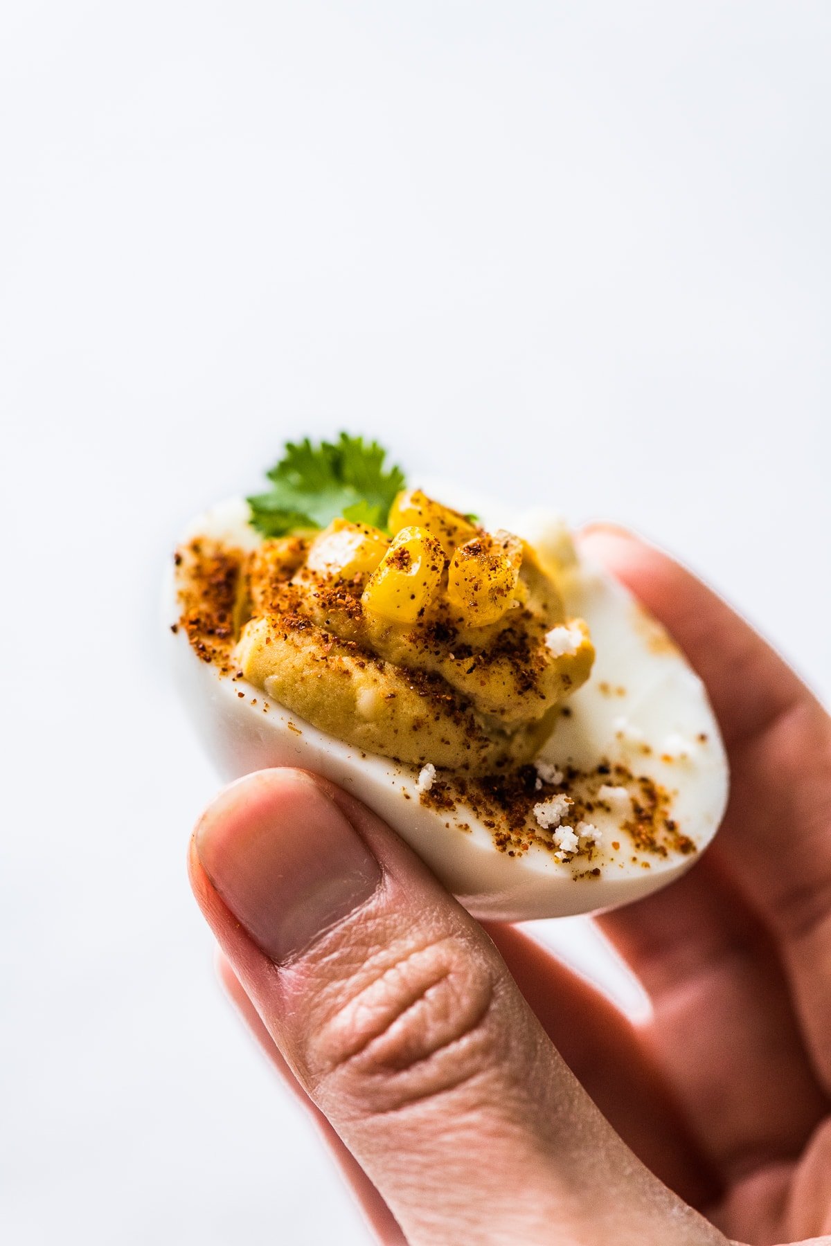 A hand holding a Mexican street corn deviled egg.