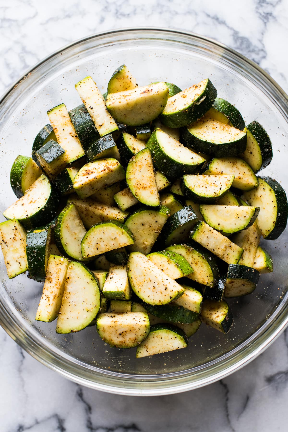 Sliced zucchini in a bowl tossed with spices.