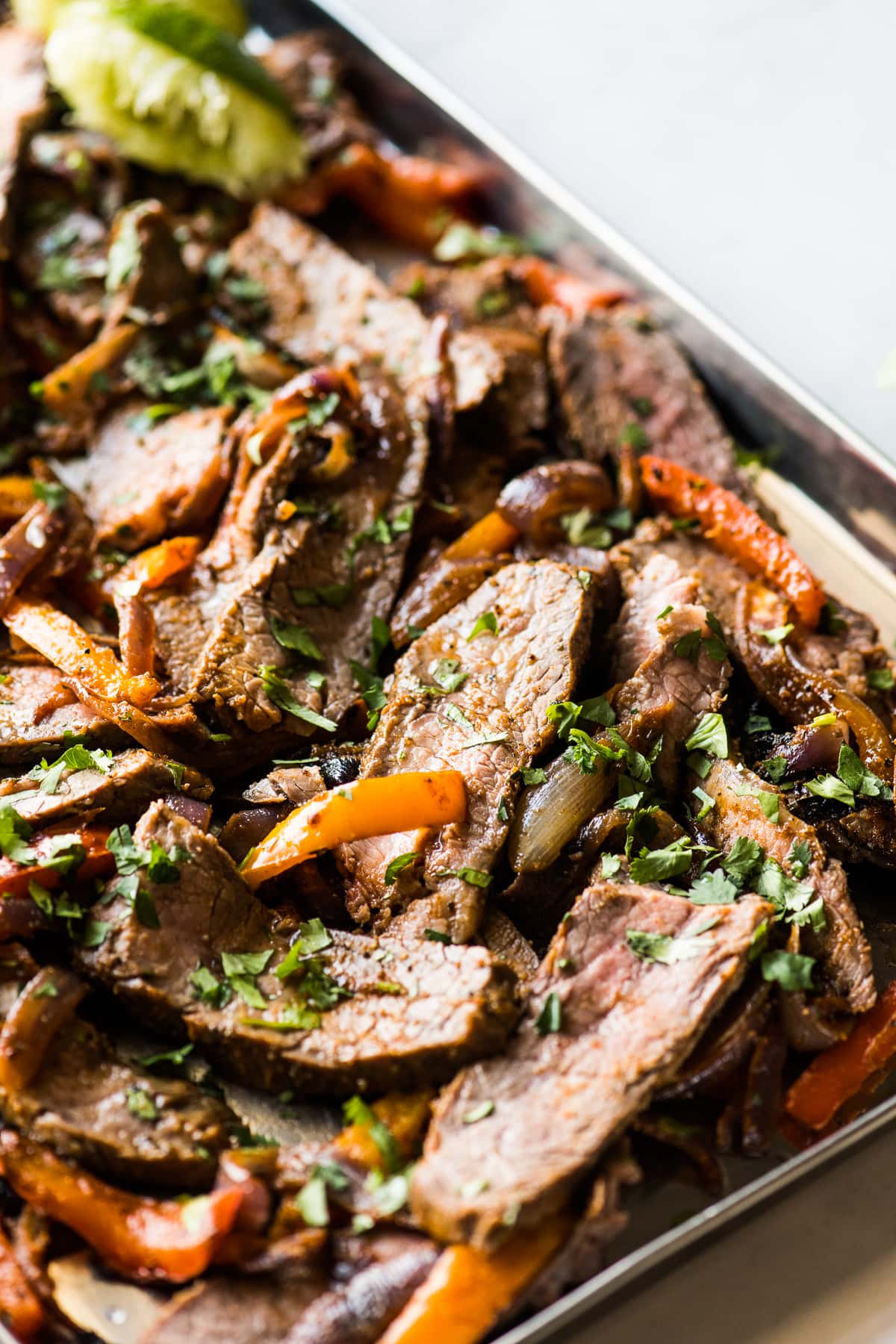 Sliced steak fajitas with peppers and onions on a sheet pan.