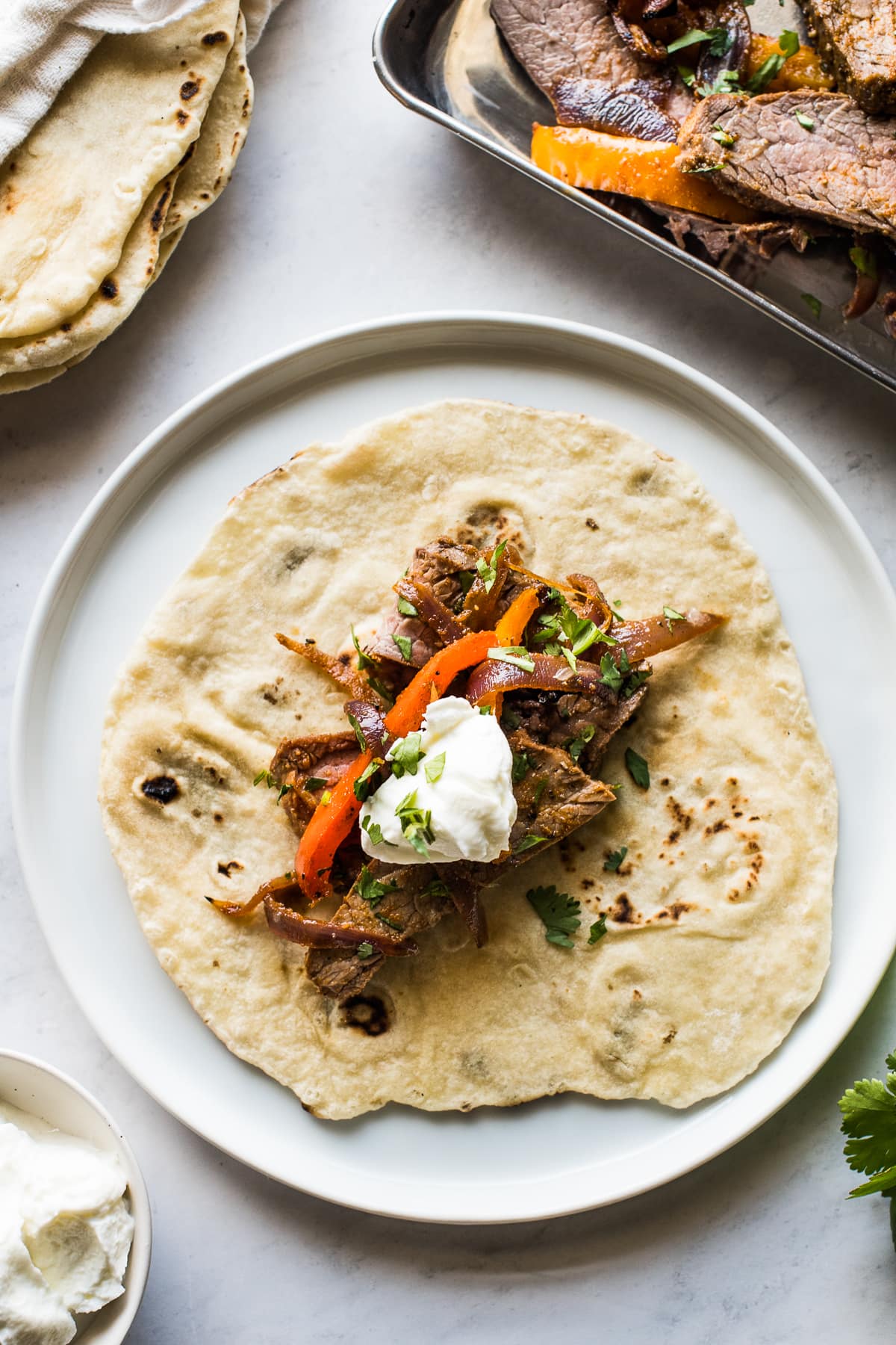 Sheet pan steak fajitas on a flour tortilla topped with sour cream and cilantro.