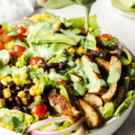 Cilantro-lime dressing being poured on a bowl of southwest chicken salad.