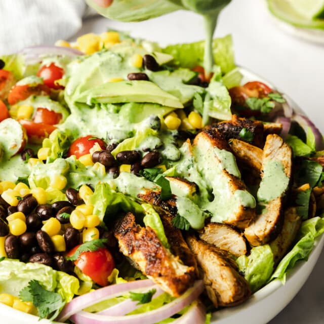 Cilantro-lime dressing being poured on a bowl of southwest chicken salad.