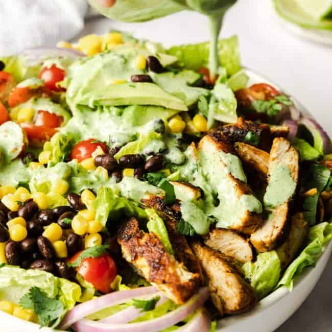 Cilantro-lime dressing being poured on a bowl of southwest chicken salad.