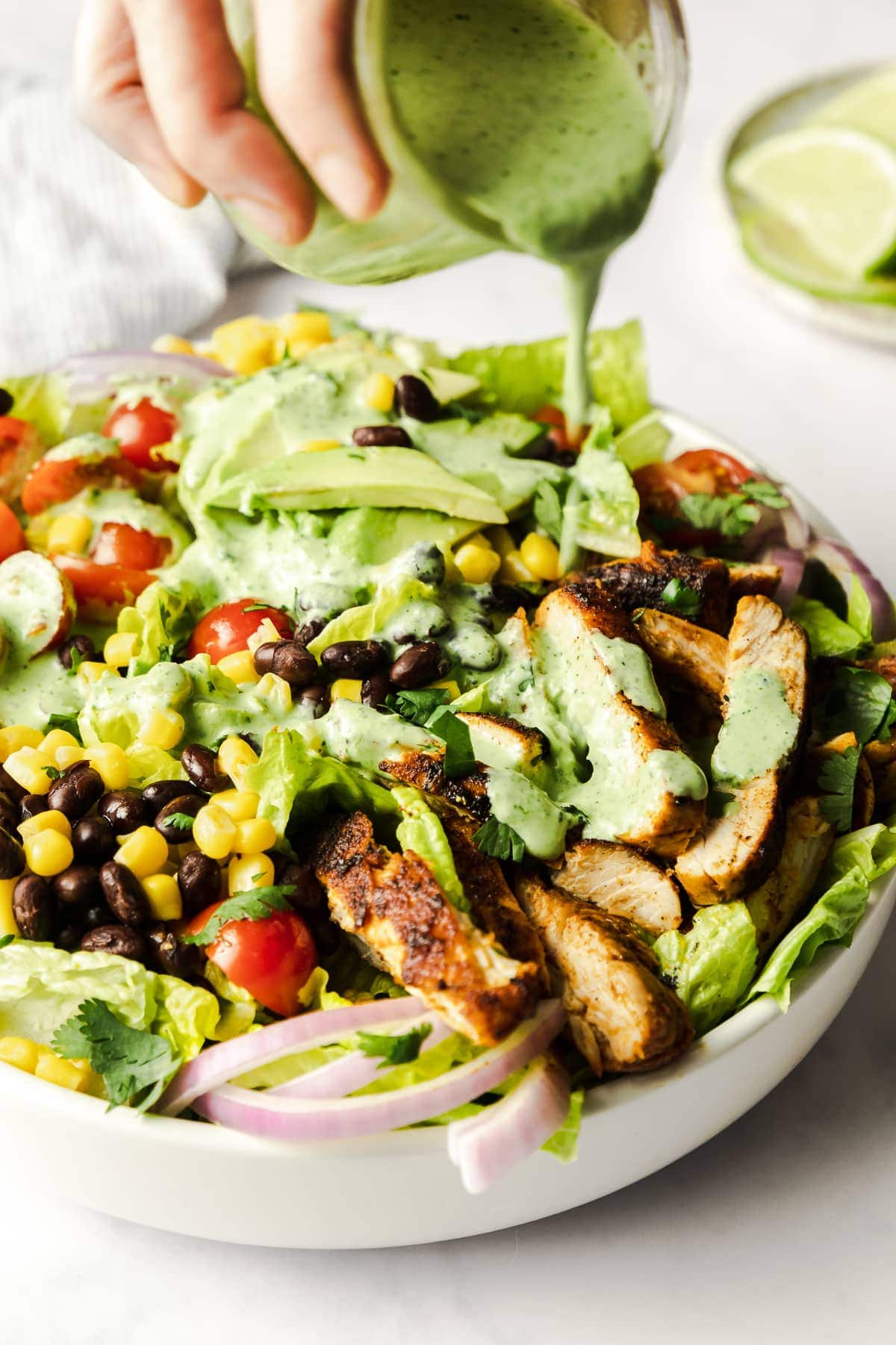 Cilantro-lime dressing being poured on a bowl of southwest chicken salad.