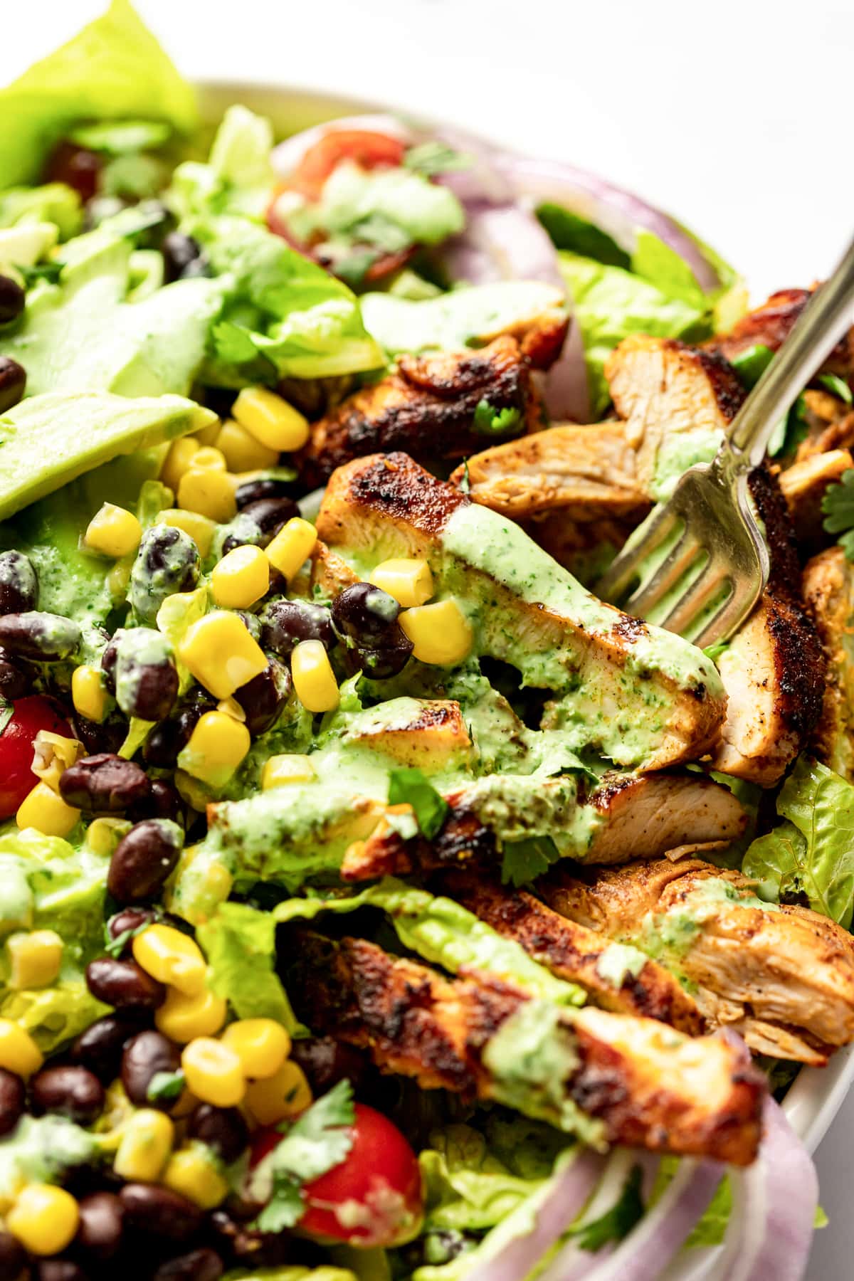 A fork digging into a slice of chicken in a Southwest Chicken Salad bowl.