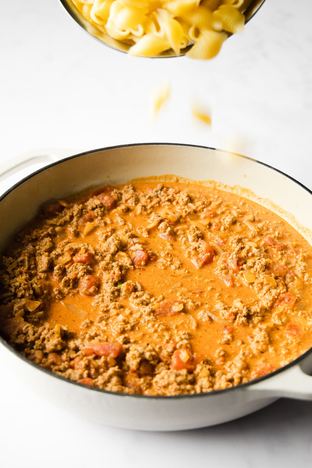 Pouring pasta into a skillet.