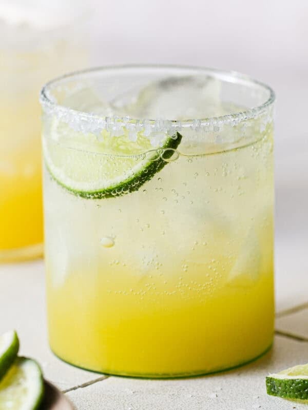 A virgin margarita mocktail in a glass with a lime wedge on a table.