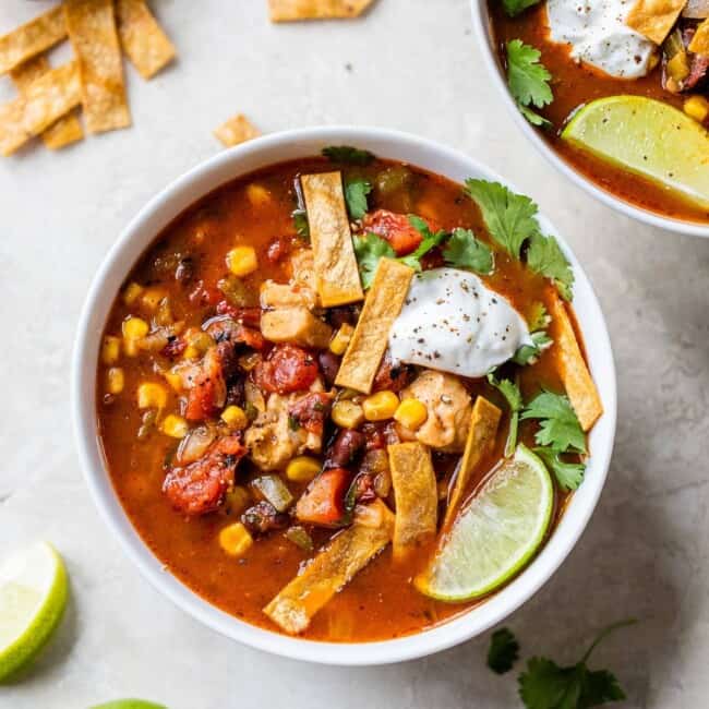 A bowl of southwest chicken soup topped with tortilla strips and sour cream.