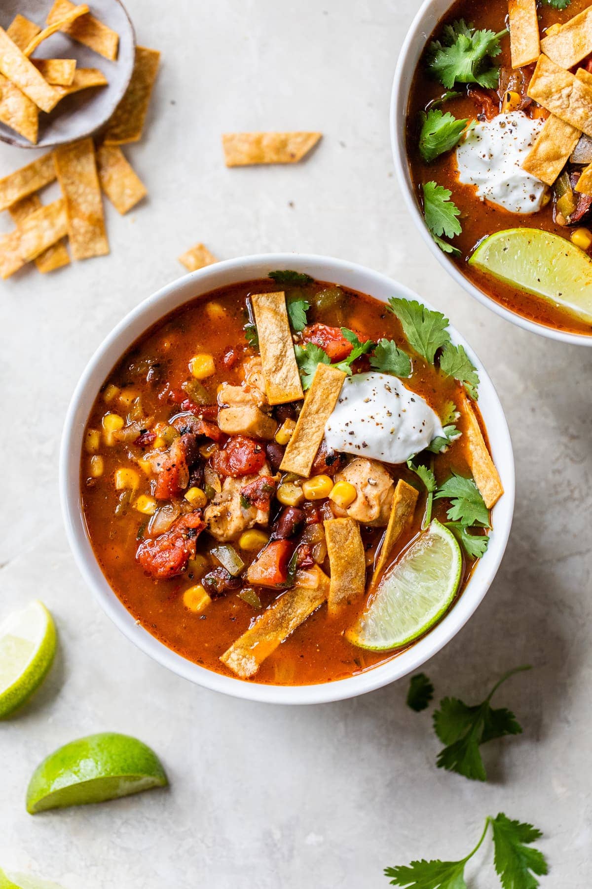 A bowl of southwest chicken soup topped with tortilla strips and sour cream.