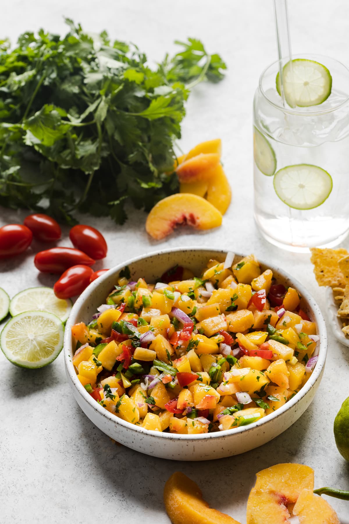 A table with a bowl of peach salsa next to slices of fresh peaches.