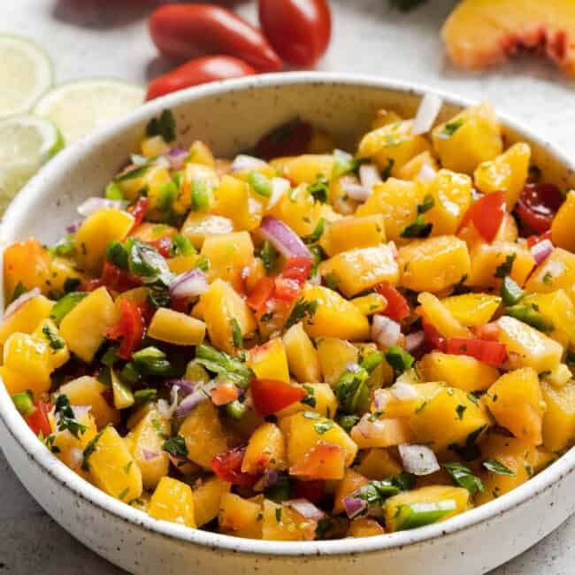 Fresh peach salsa in a bowl next to tortilla chips.