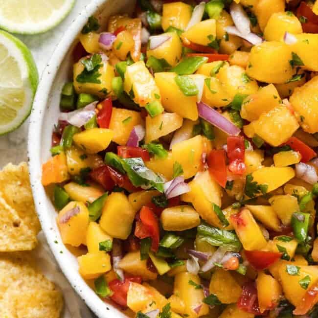 A bowl of peach salsa topped with cilantro and served with tortilla chips.