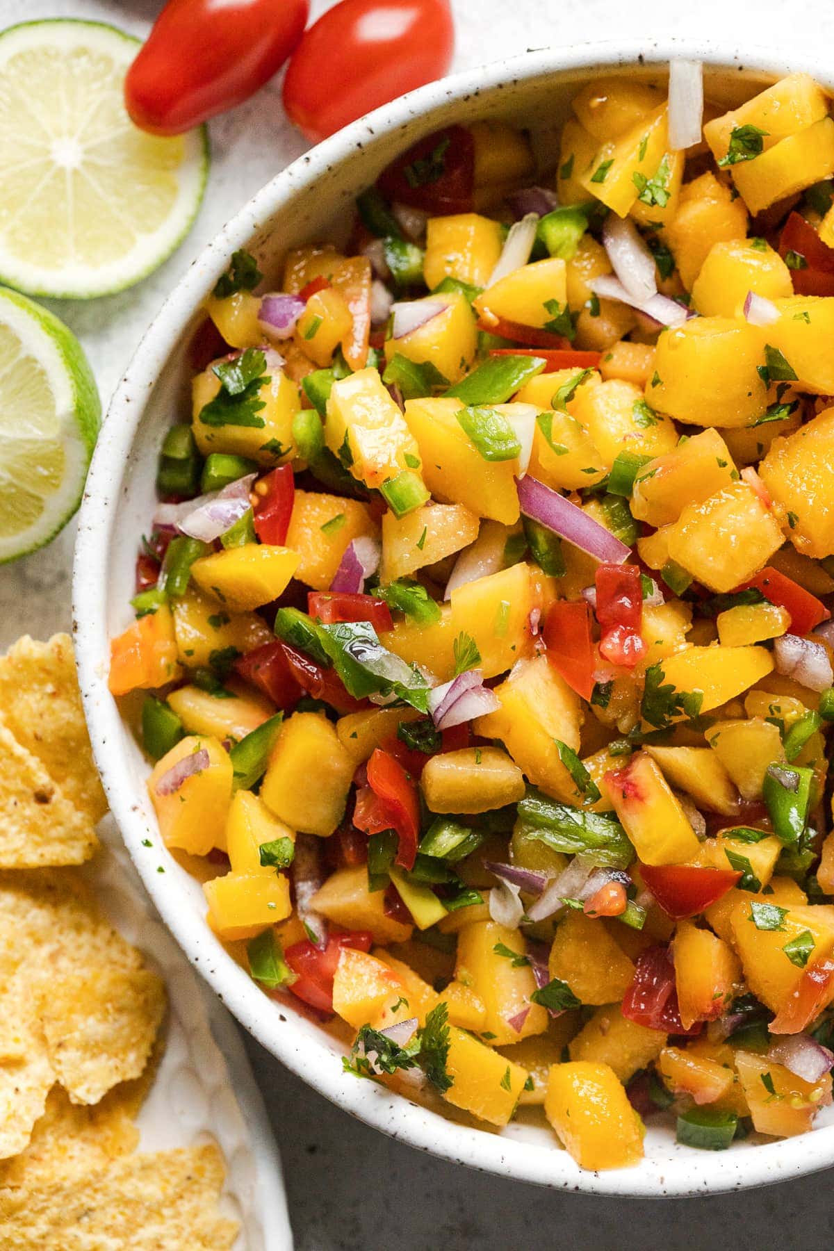 A bowl of peach salsa topped with cilantro and served with tortilla chips.