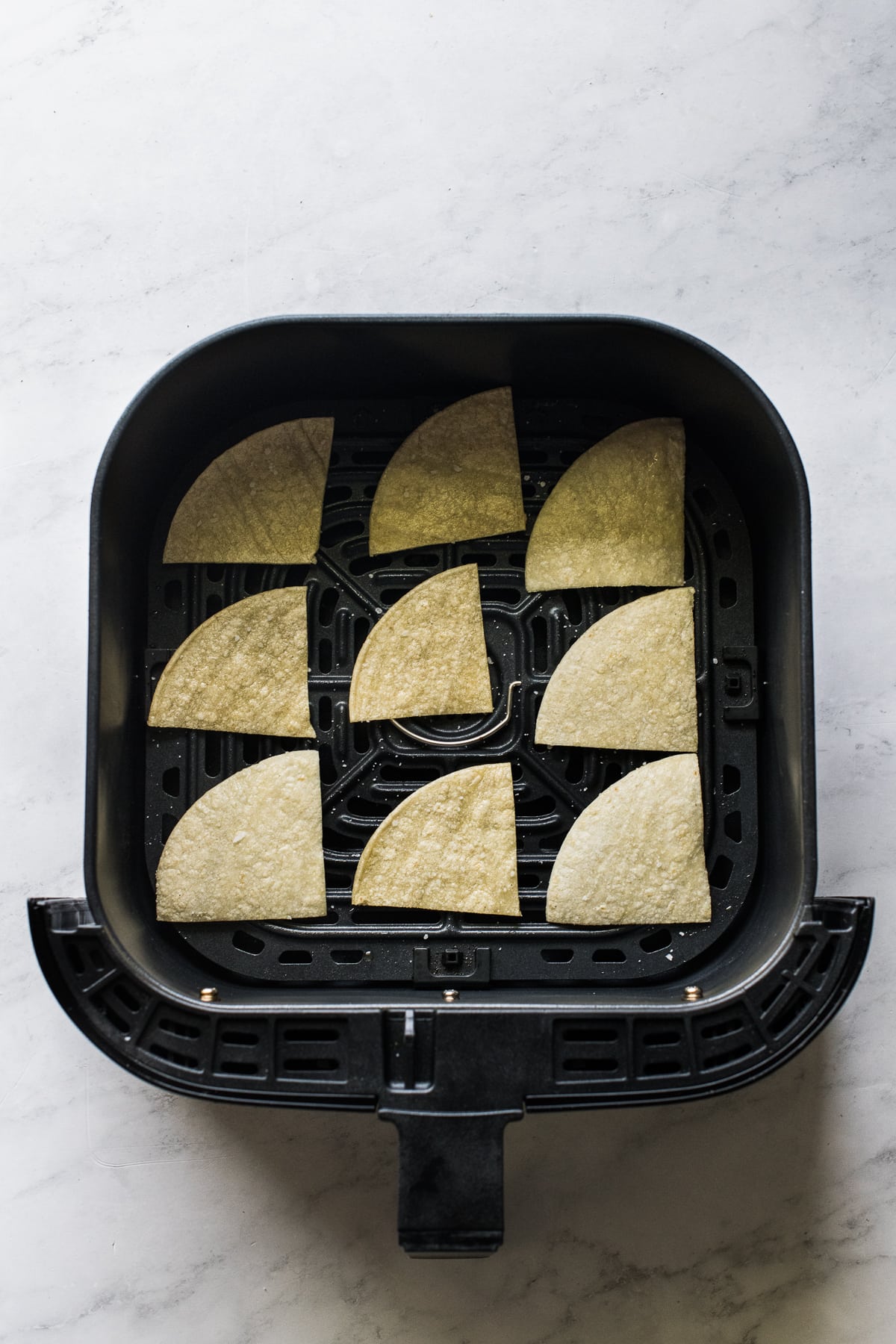 Corn tortillas cut into chips in the basket of an air fryer.