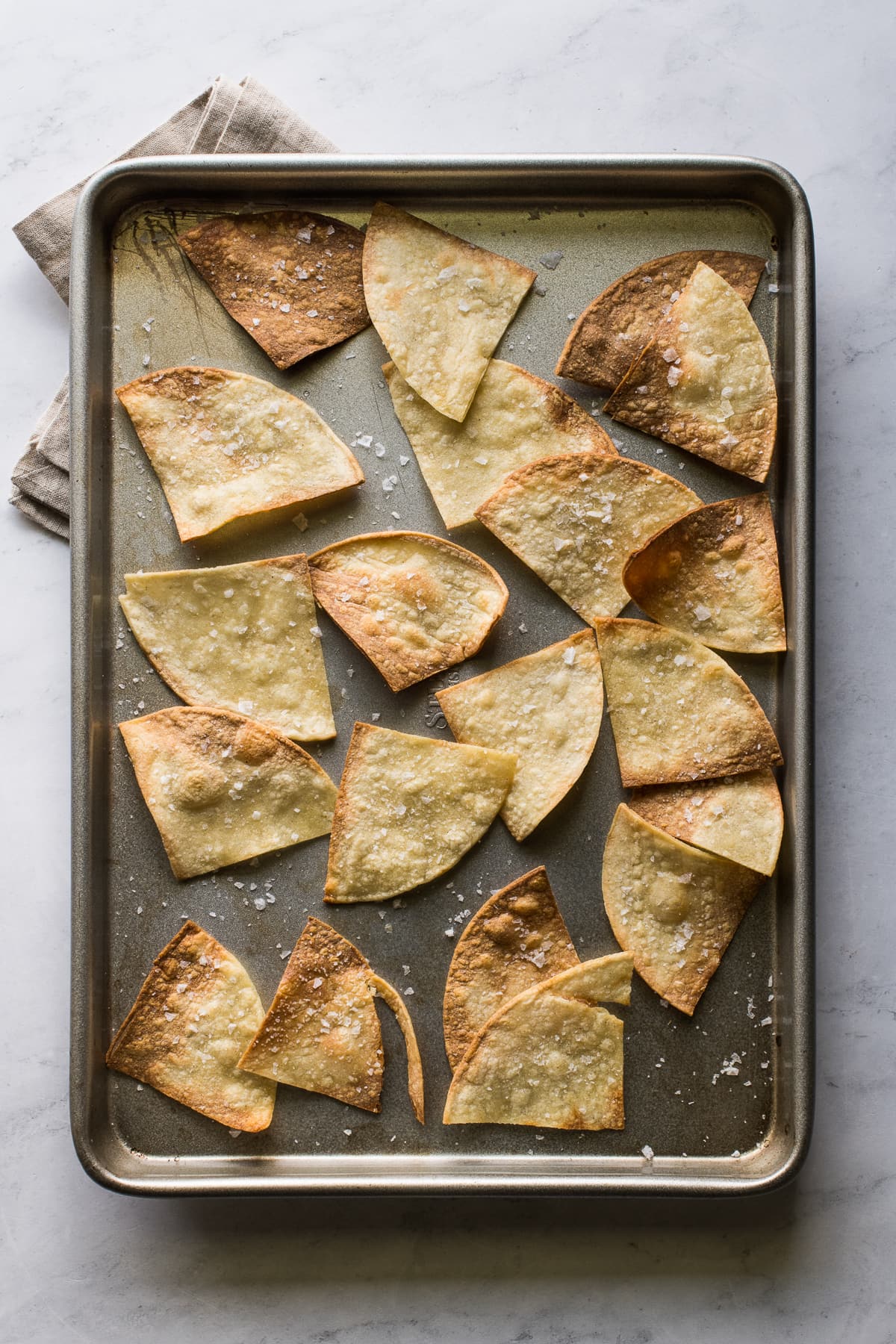 Air fried tortilla chips on a baking sheet seasoned with salt.