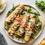 Beef taquitos topped with sour cream, avocado, and tomatoes.