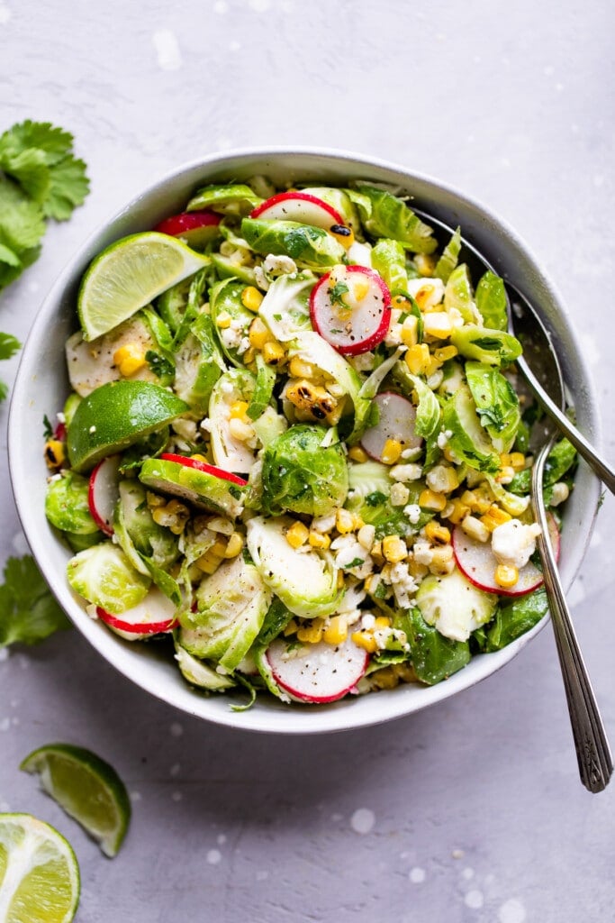 Mexican Brussels Sprout Salad topped with sliced radishes and lime wedges.