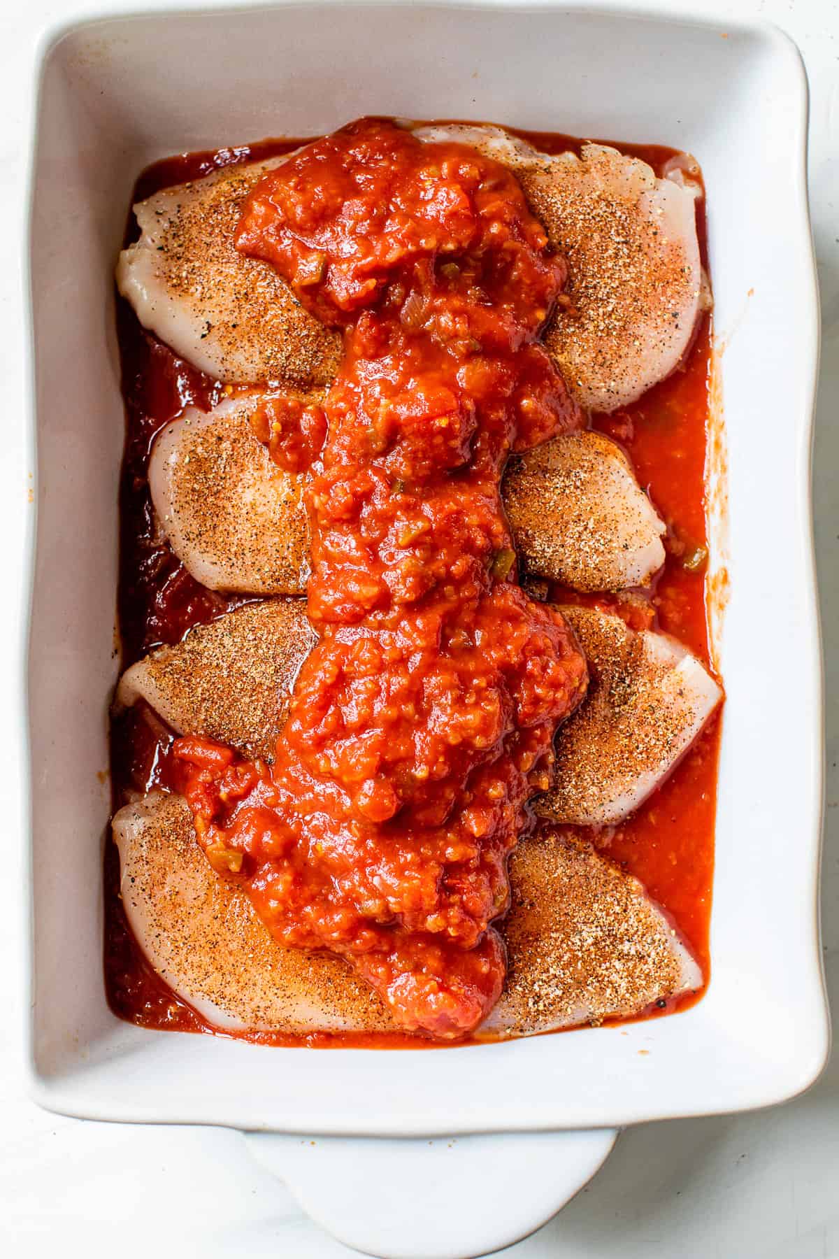 Seasoned chicken breast topped with chunky salsa in a baking dish