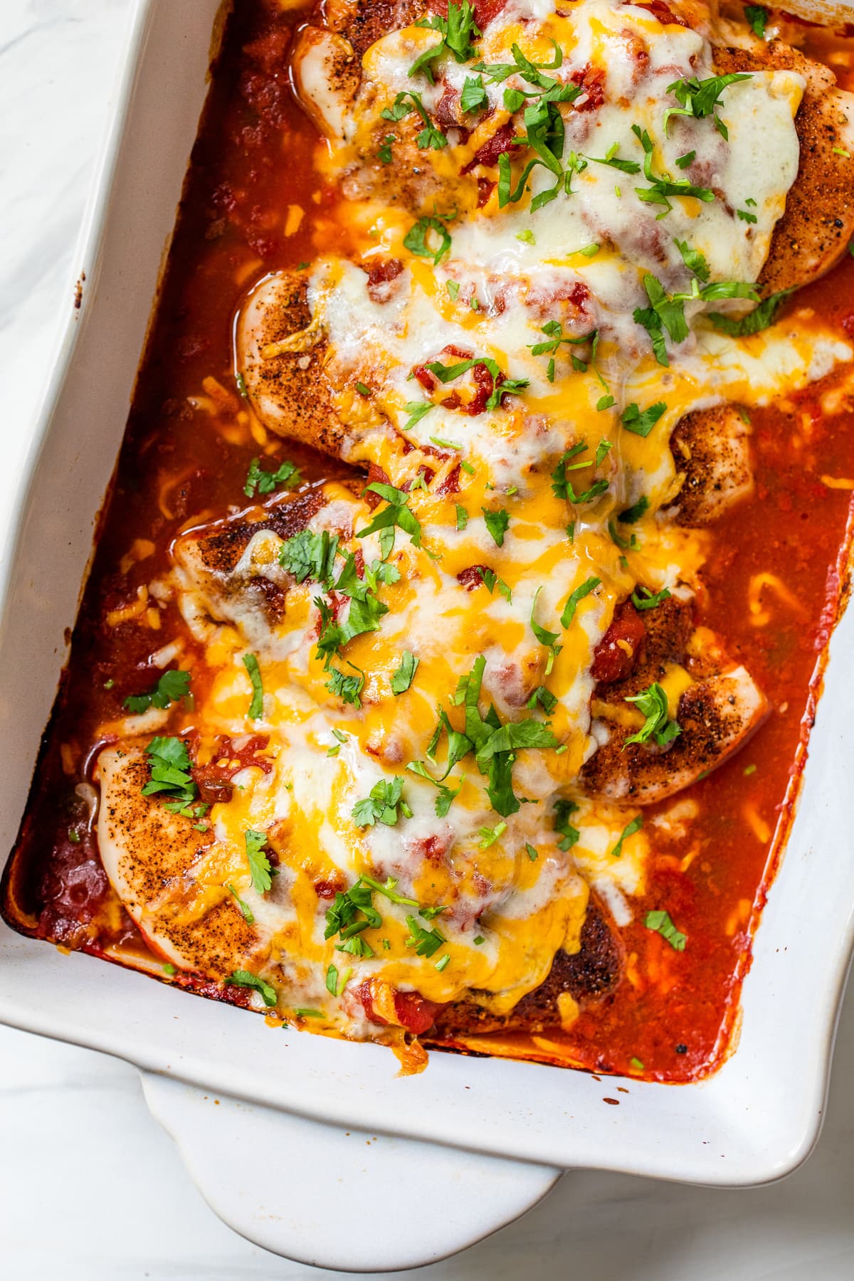 Salsa chicken in a baking dish topped with melted cheese and fresh cilantro.