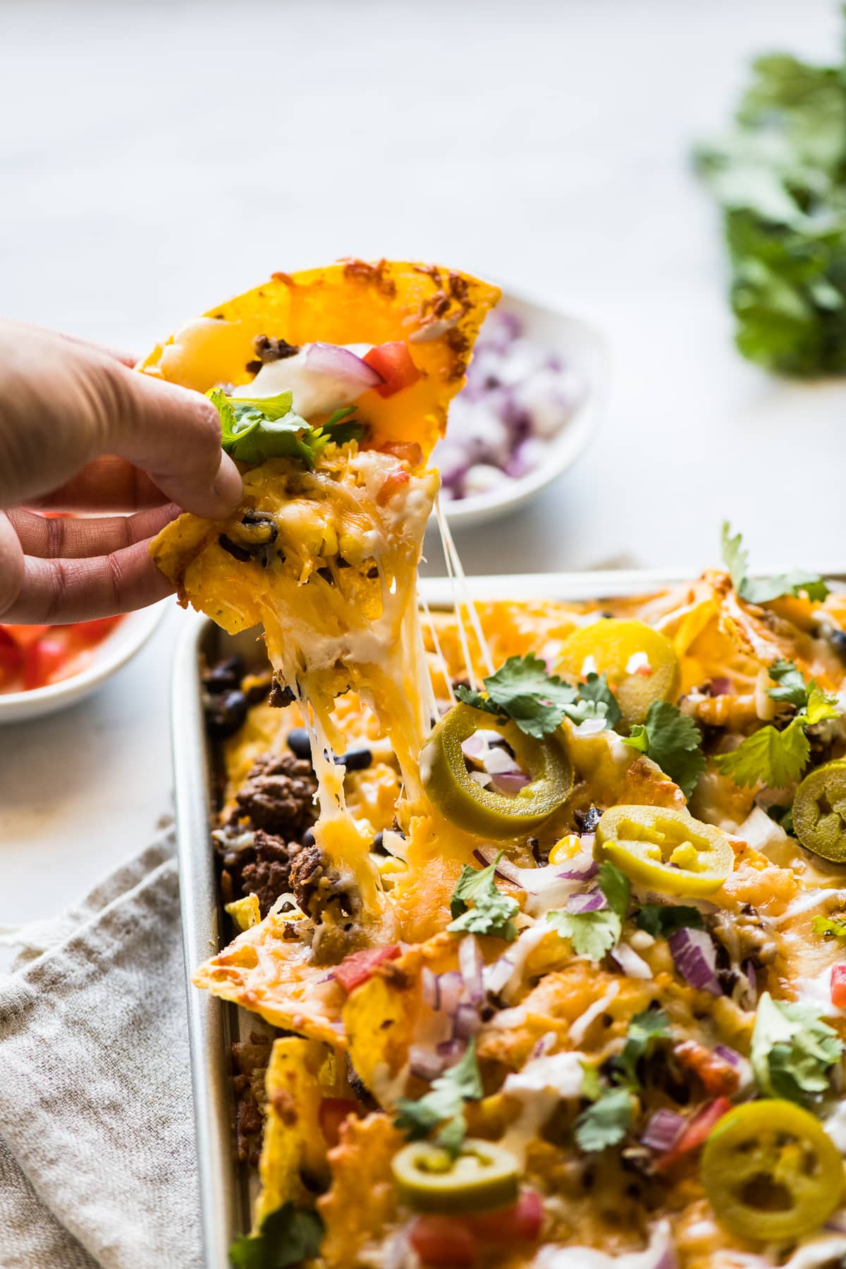 A tortilla chip topped with melted cheese being pulled off a pan of sheet pan nachos.