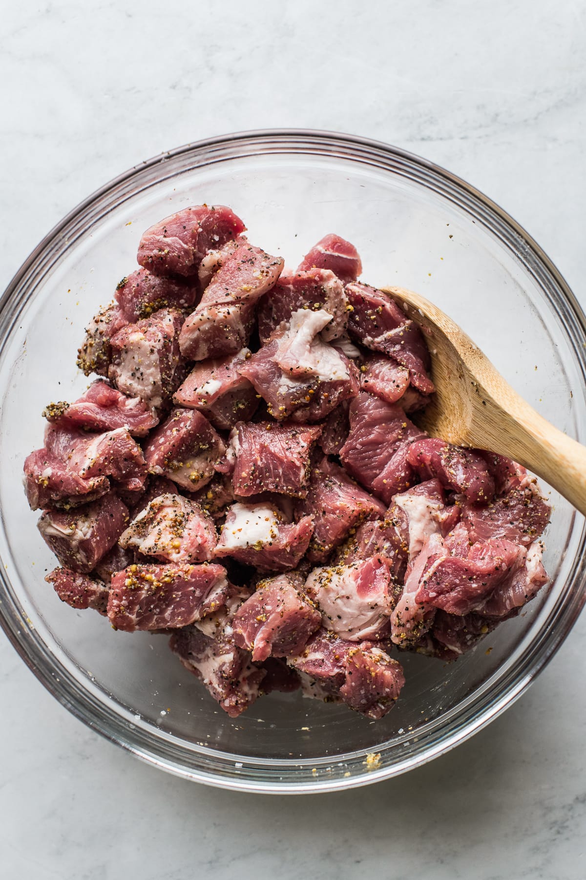Chunks of pork shoulder in a bowl seasoned with salt, pepper, and coarse-ground mustard.