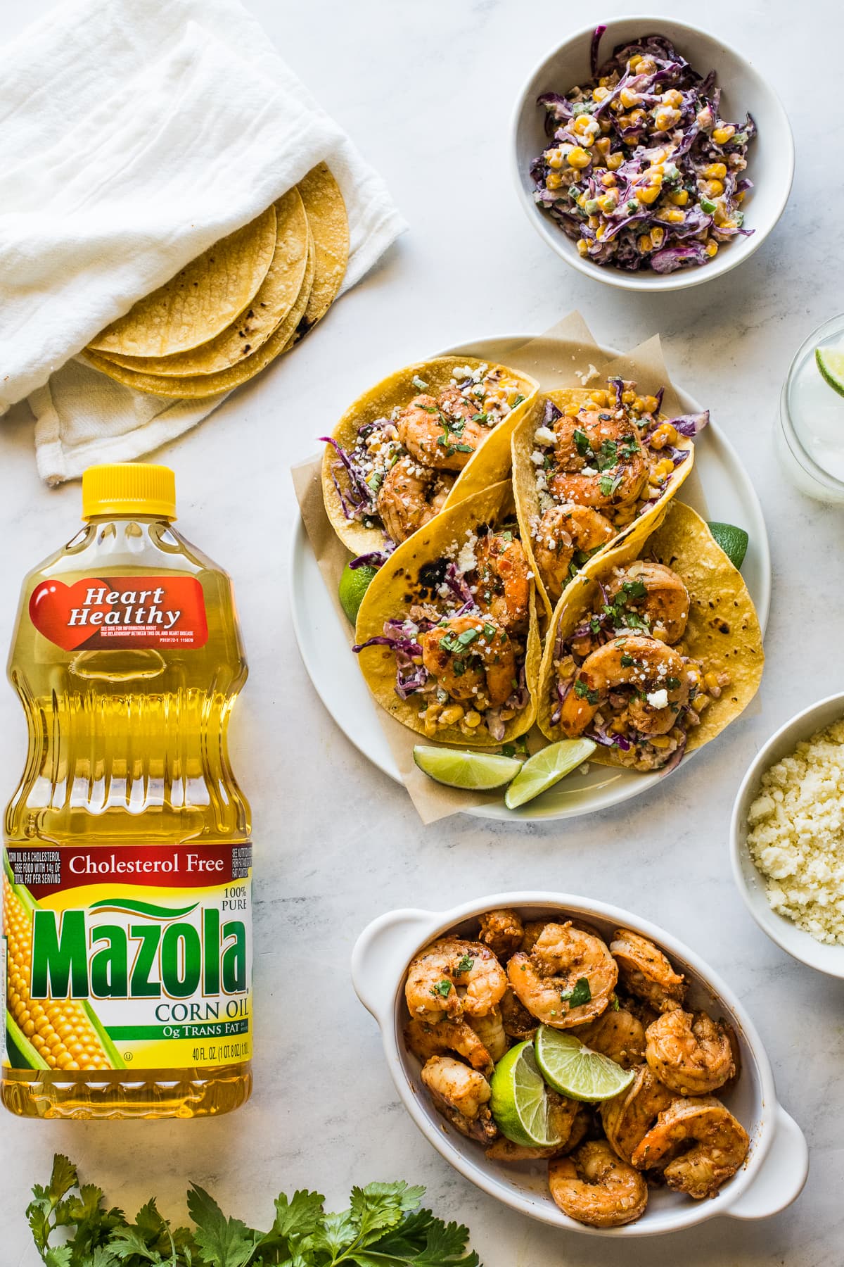 Spicy shrimp tacos on a plate next to corn tortillas, elote slaw, cotija cheese, and more.