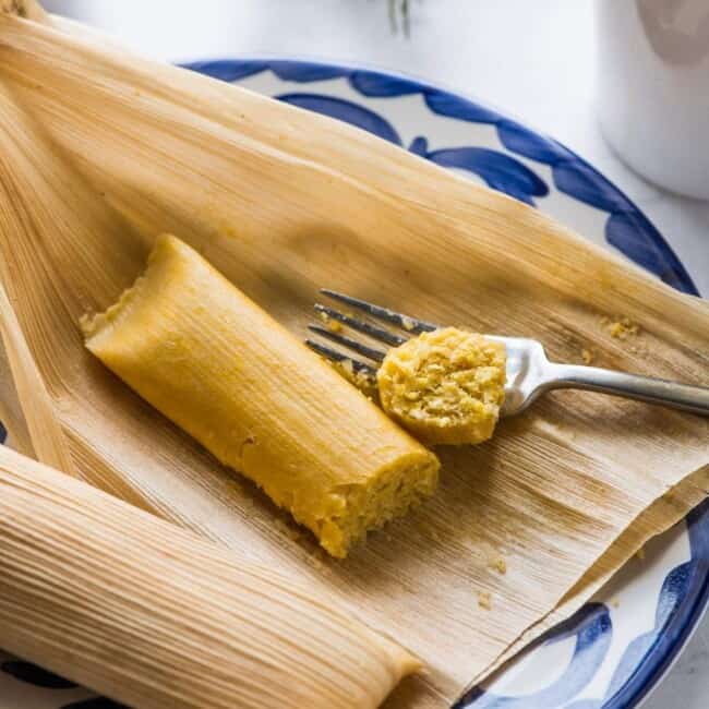 A cooked sweet corn tamale on a plate next to a cup of coffee.