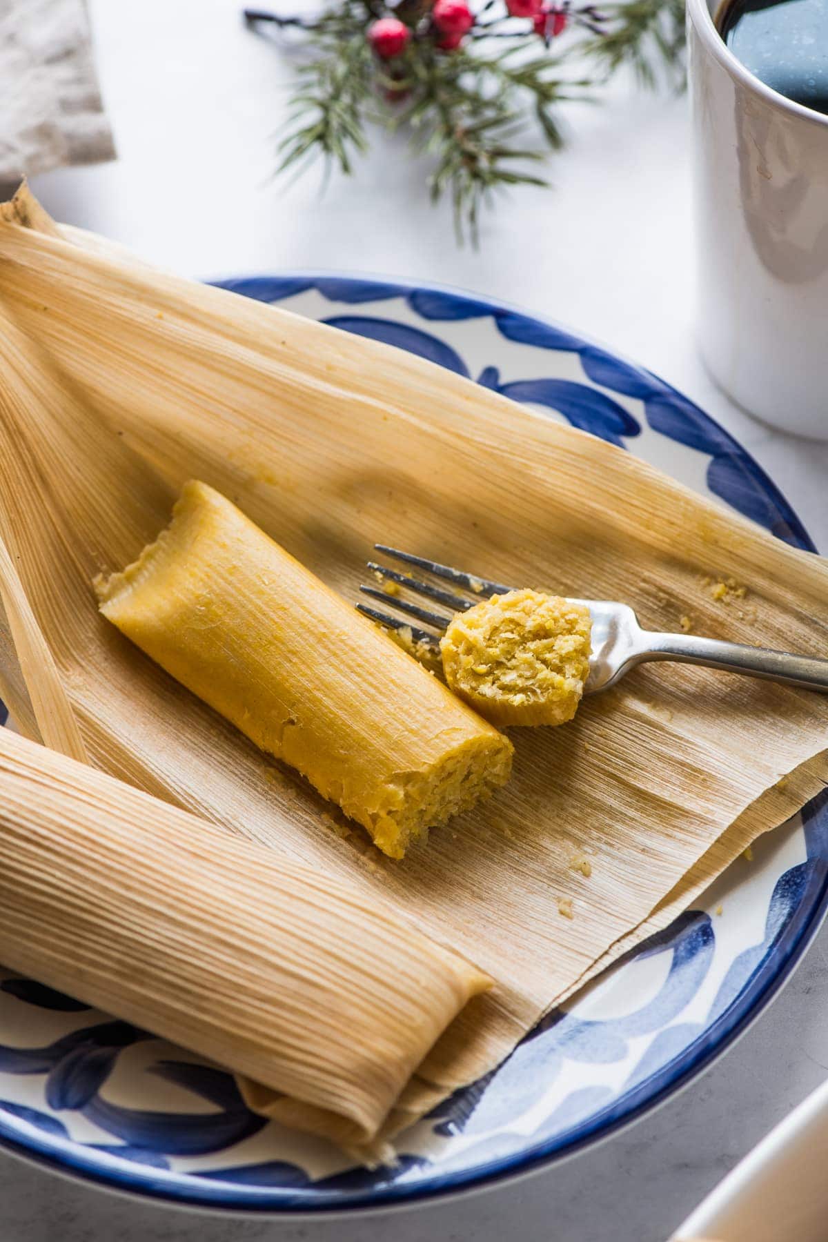 A cooked sweet corn tamale on a plate next to a cup of coffee.