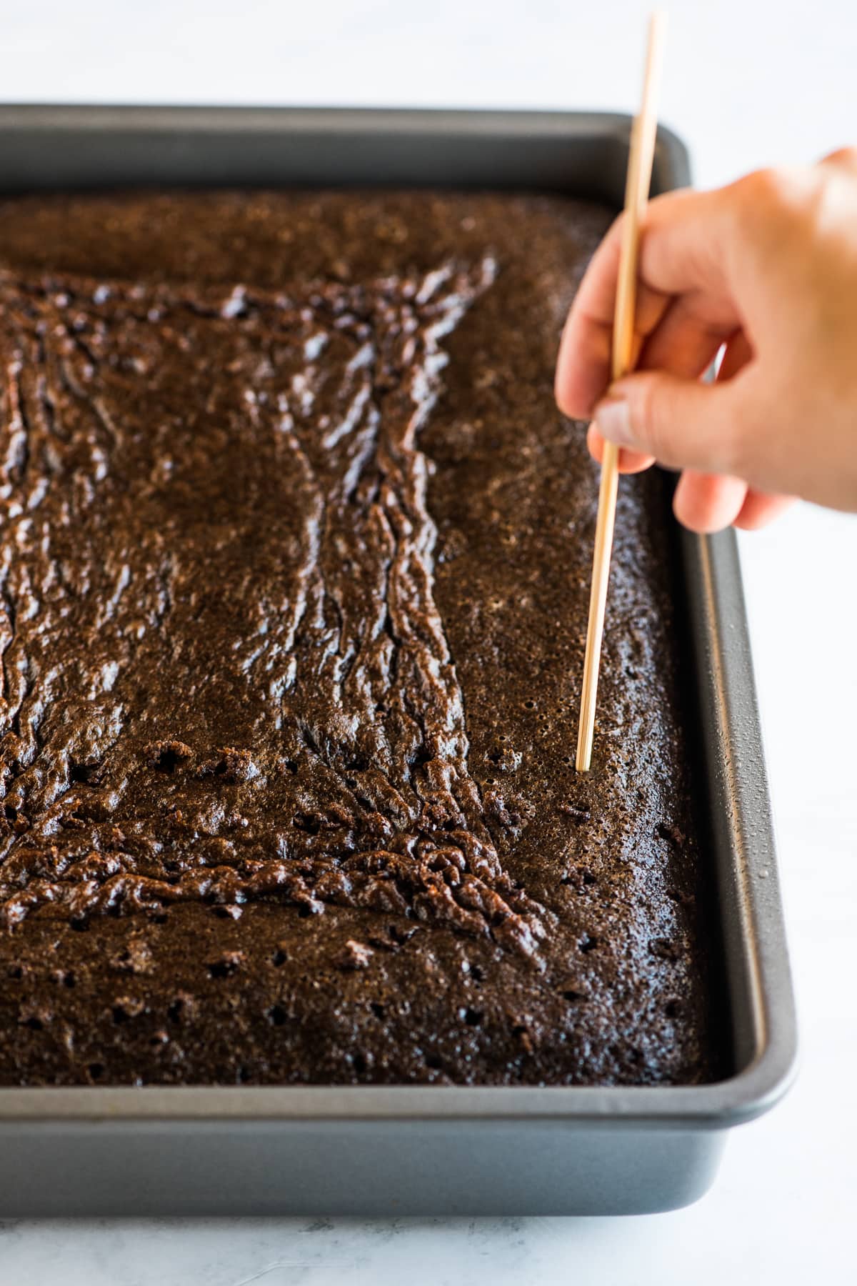 Poking holes in a tres leches cake with a skewer.