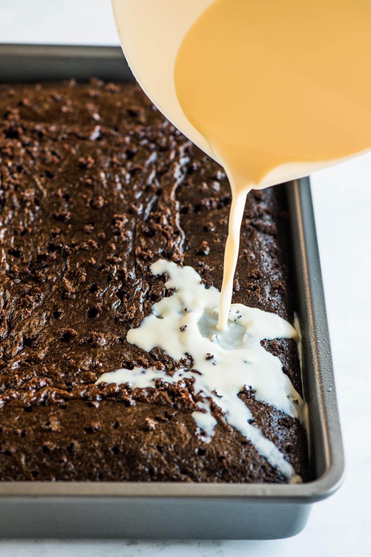 Pouring a 3 milk mixture on top of a tres leches cake.