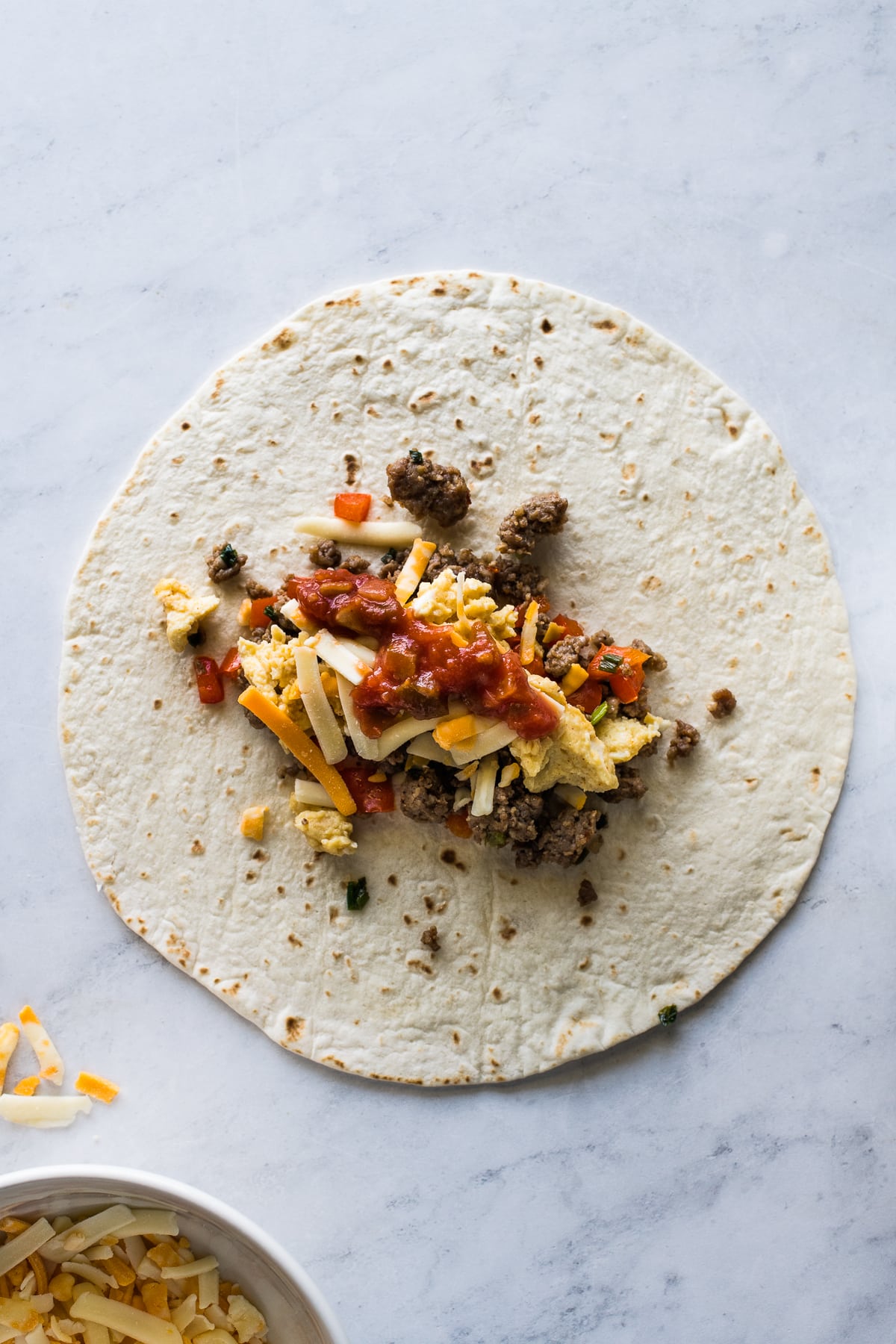 A flour tortilla with breakfast sausage, scrambled eggs, salsa, and cheese.
