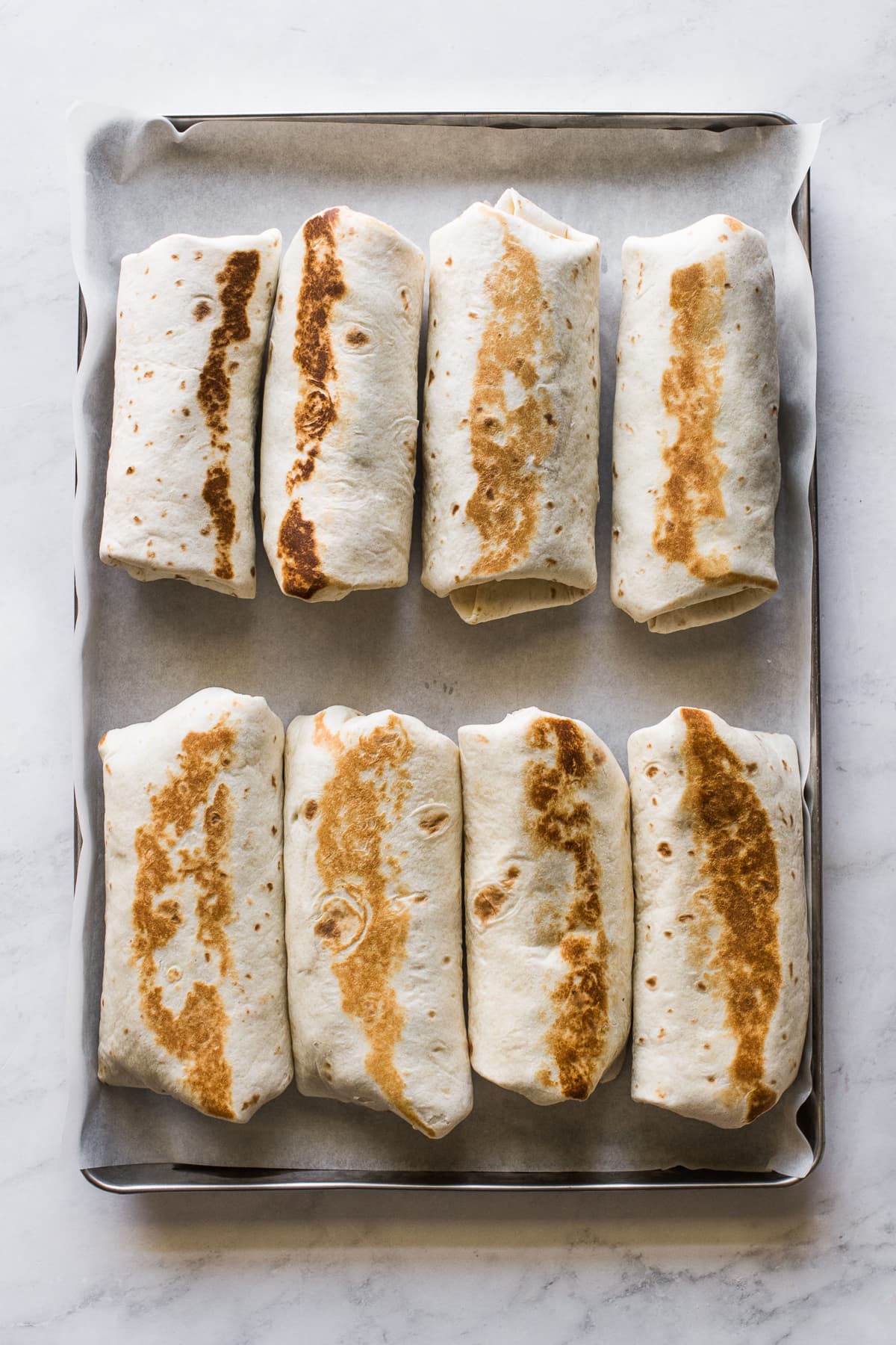 Breakfast burritos rolled and sealed on a sheet pan ready to serve.